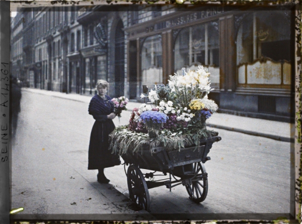 Une marchande de fleurs, en face du 53 rue Cambon, Paris, 1er arr., France, 1918, autochrome , 9×12 cm, Paris, collections du musée Albert-Kahn, inv. A14361 (domaine public, licence CC-00)